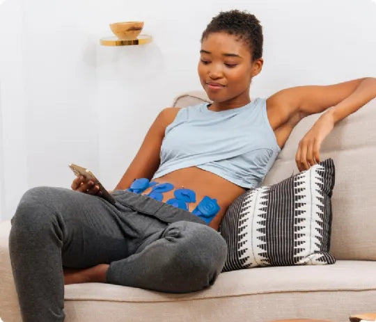 Woman using PowerDot 2.0 Duo on abdomen for pain relief at home